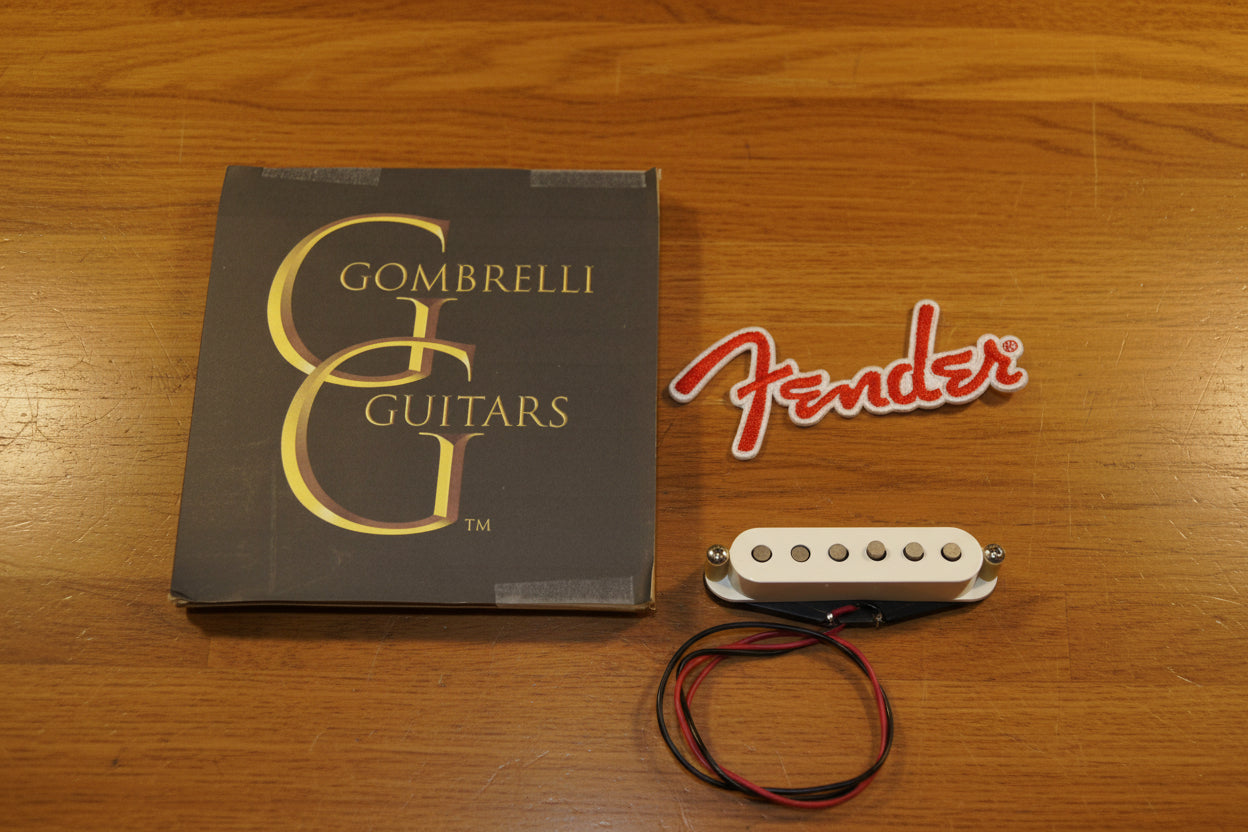 Fender Gombrelli humbucker guitar pickup with black and red wires, shown next to its original Gombrelli Guitars box and a red Fender logo decal on a white fabric background.
