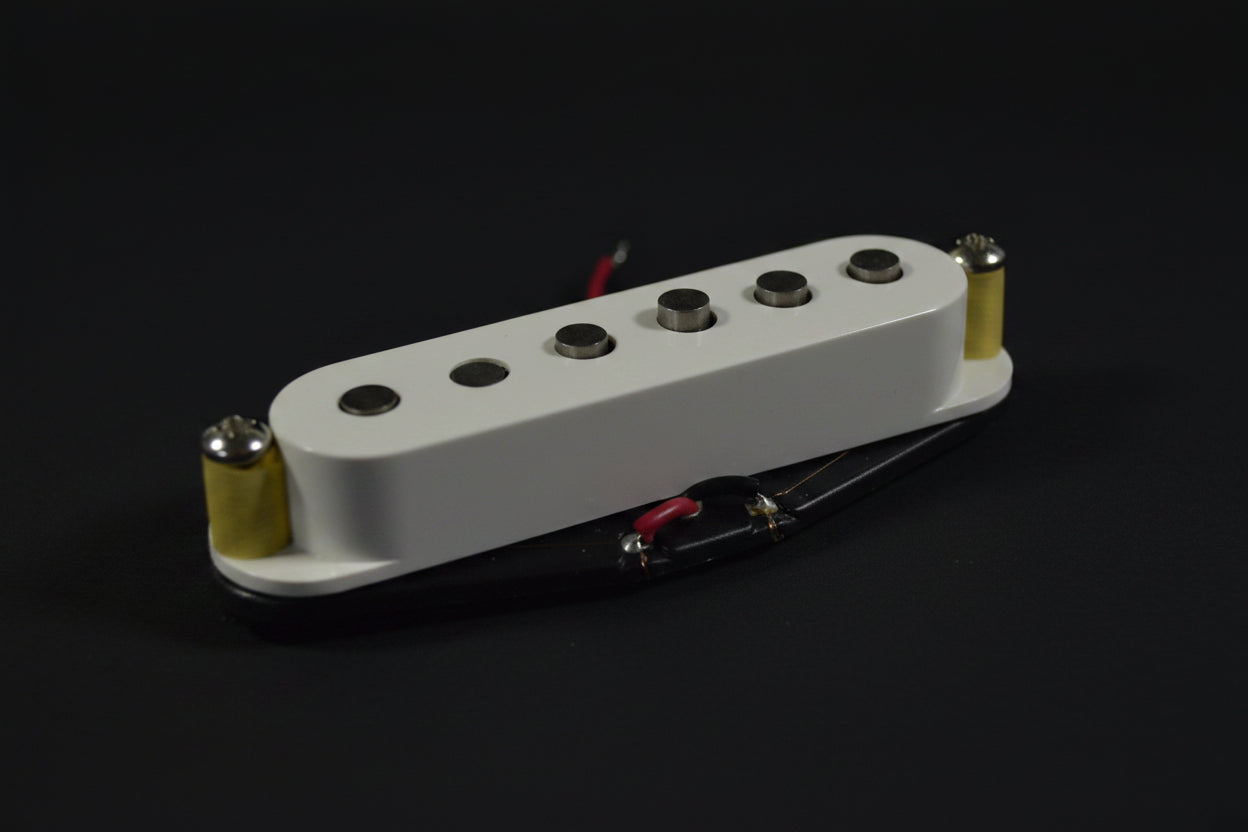 A close-up of a white Fender humbucker guitar pickup with gold and black hardware, resting on a white fabric background with a red embroidered Fender logo.