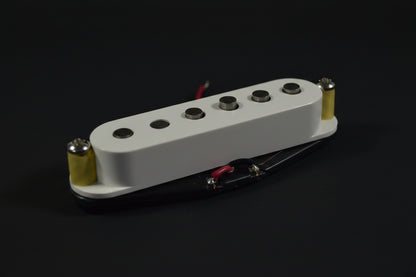 A close-up of a white Fender humbucker guitar pickup with gold and black hardware, resting on a white fabric background with a red embroidered Fender logo.