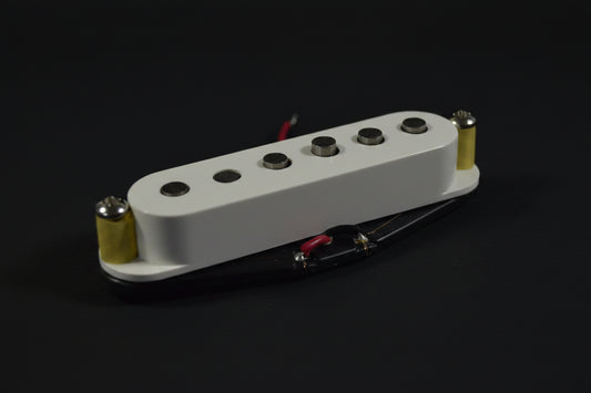 A close-up of a white Fender humbucker guitar pickup with gold and black hardware, resting on a white fabric background with a red embroidered Fender logo.