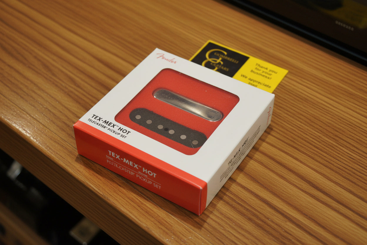 Fender Tex-Mex Hot Telecaster Pickup Set in its original white and red retail box, featuring a window showing the red and brown pickups, with a gold G&G sticker on a black textured background.
