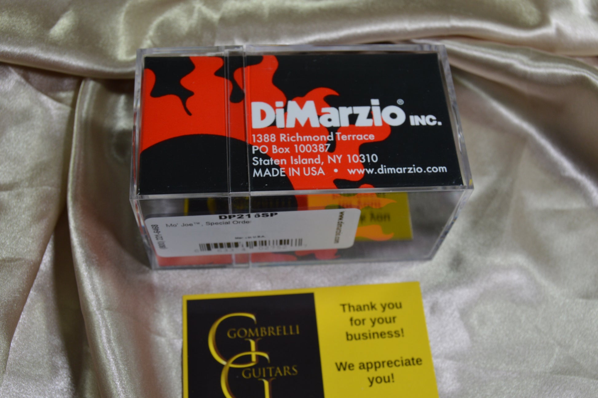 A clear plastic case containing DiMarzio Inc. DW-2105 DSP wound wire for electric guitars, placed on a draped champagne satin fabric next to a yellow Gombrelli Guitars thank you card.