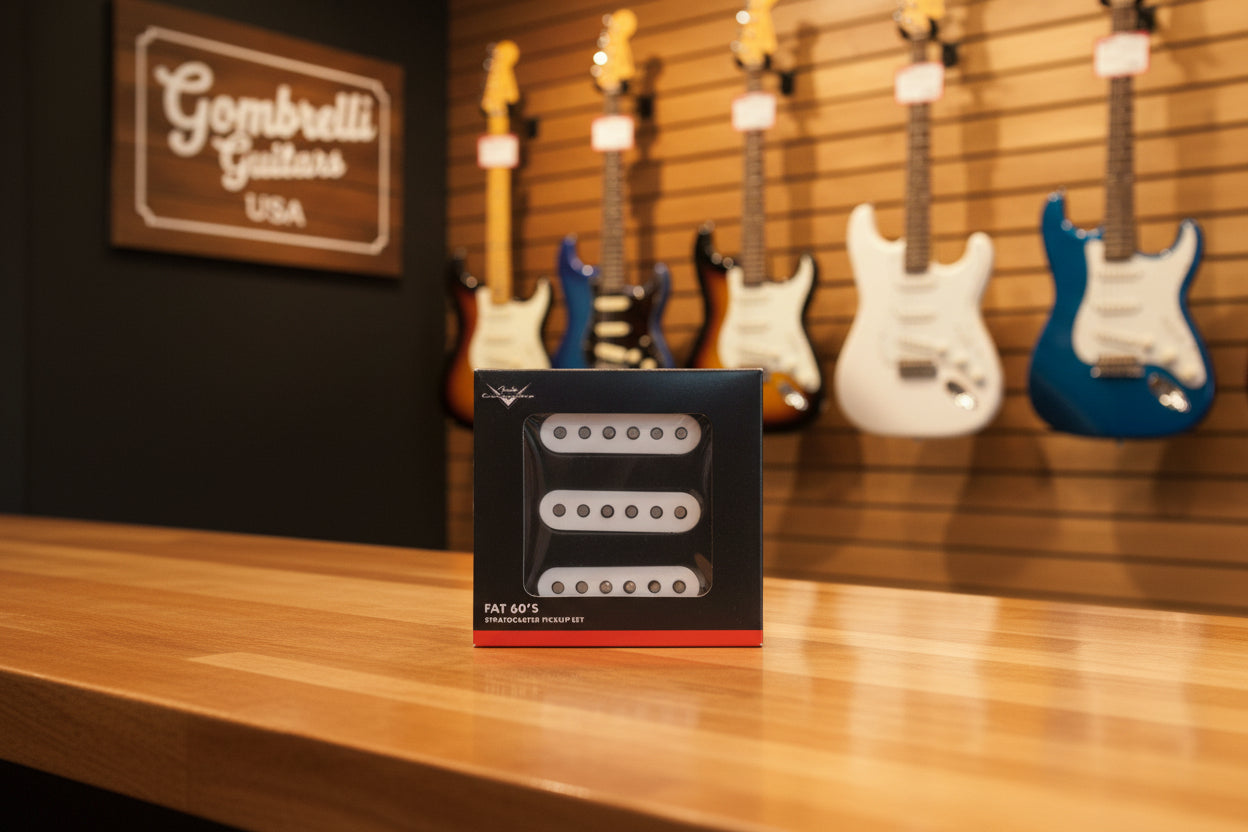 A package of three white Fat 60's Stratocaster pickup coils in a black box with a red stripe at the bottom, placed on a dark textured surface.