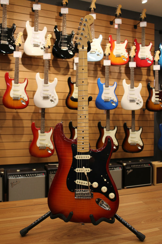 A Fender electric guitar with a sunburst red body and black pickguard, resting on a black fabric backdrop.