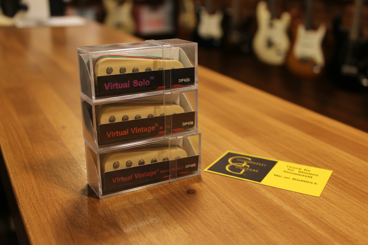 Three custom selected Dimarzio Virtual Vintage guitar pickups stacked vertically on a shiny satin fabric, with a yellow and black Gombrelli Guitars card on the right.